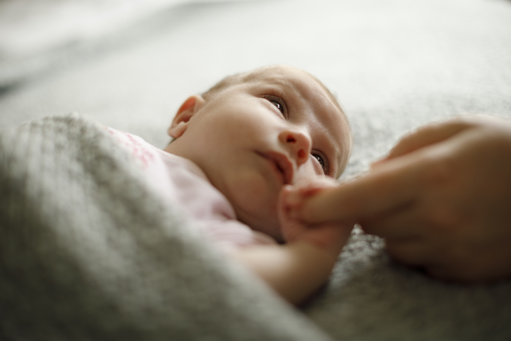 Baby lying in a crib holding an adults finger